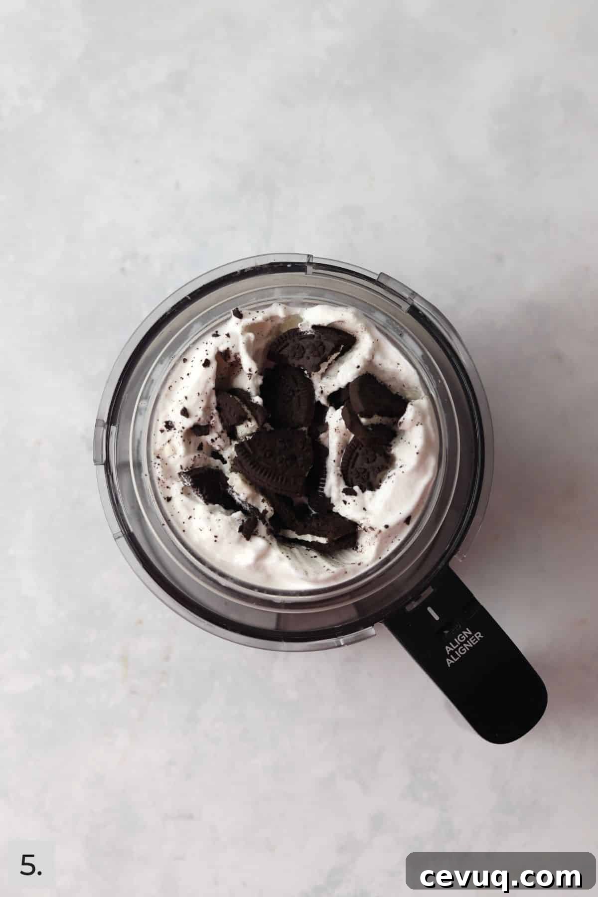 Soft serve with Oreos being added in Ninja Creami container.