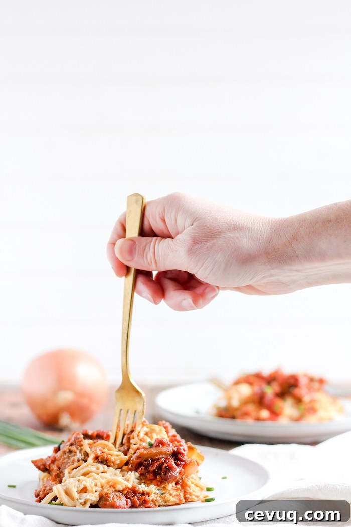 Photo shows a hand taking a bite of baked spaghetti