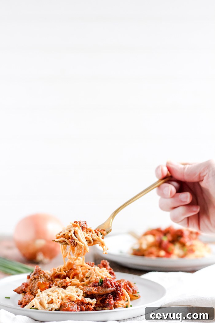 Image shows a hand taking a bite of spaghetti casserole