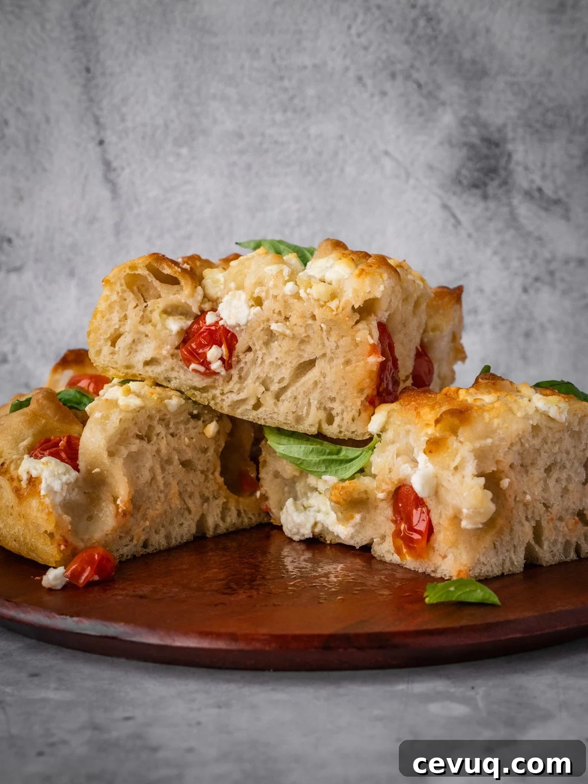 Feta and cherry tomato focaccia garnished with fresh basil on a board.