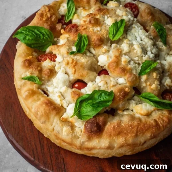 Feta and cherry tomato focaccia garnished with fresh basil on a board.