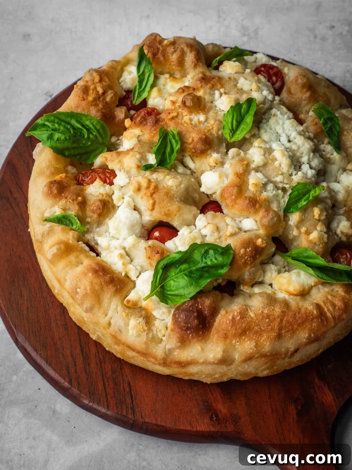 Feta and cherry tomato focaccia garnished with fresh basil on a board.