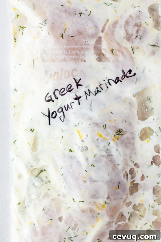 Close up of some chicken thighs covered in a white marinade in a ziploc bag that reads 'Greek Yogurt Marinade'