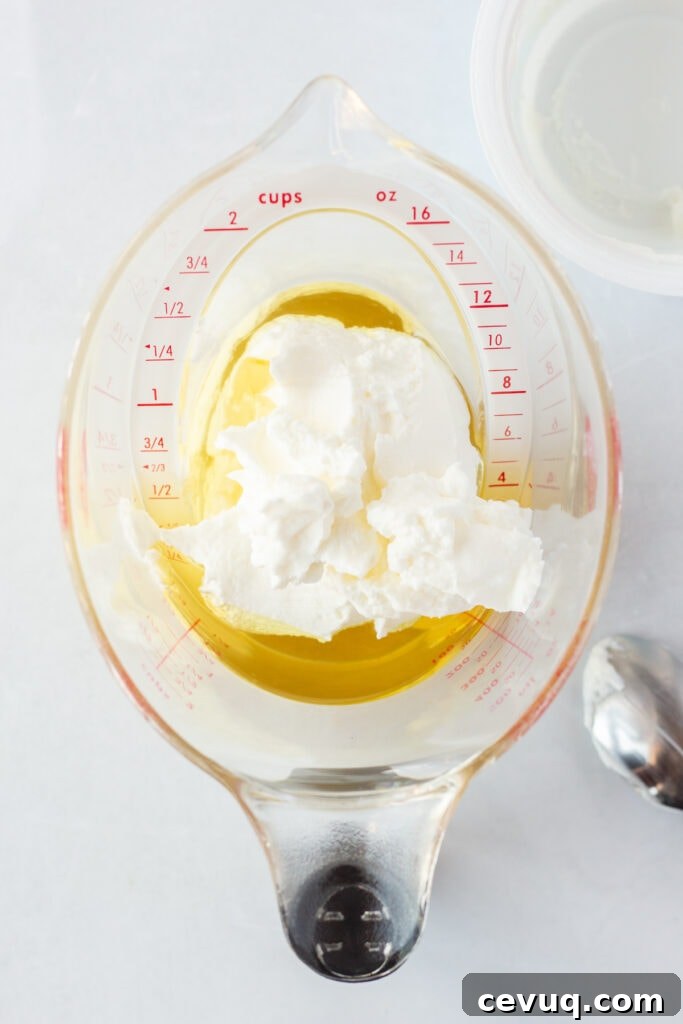 Top down shot of oil and plain Greek yogurt in a measuring cup on a white background.