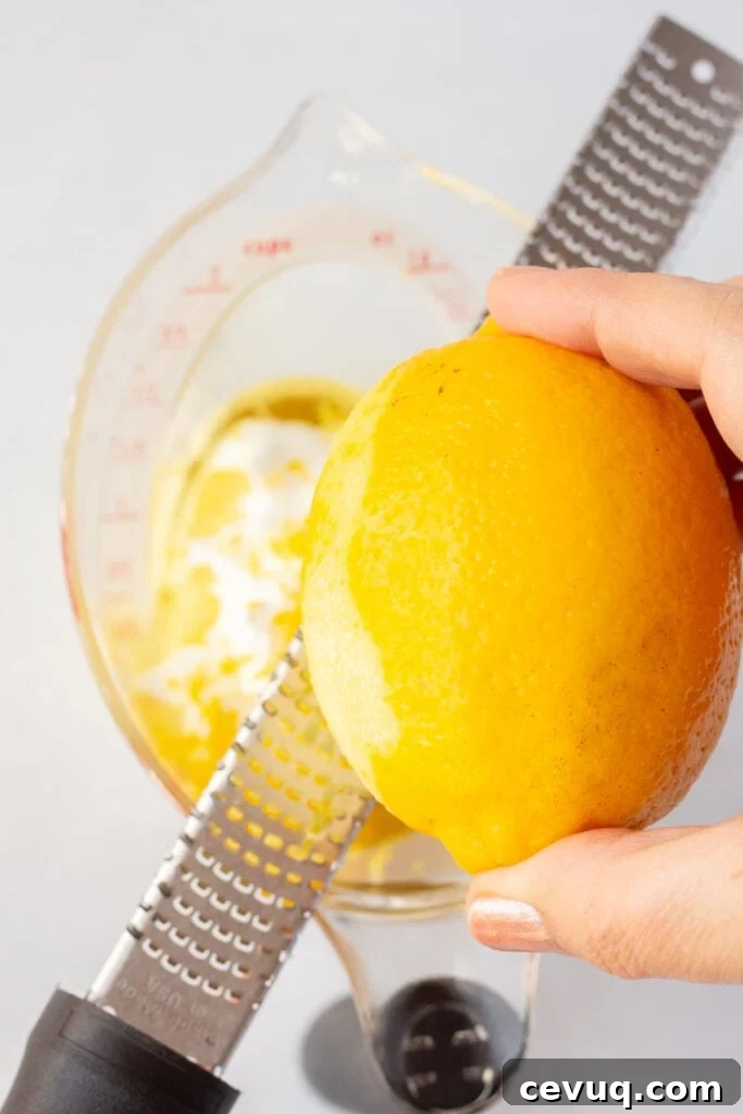 Zesting a lemon over a measuring cup with oil and yogurt already in it.