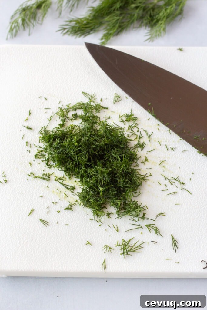 Finely chopped fresh dill fronds on a white cutting board with a knife next to them.