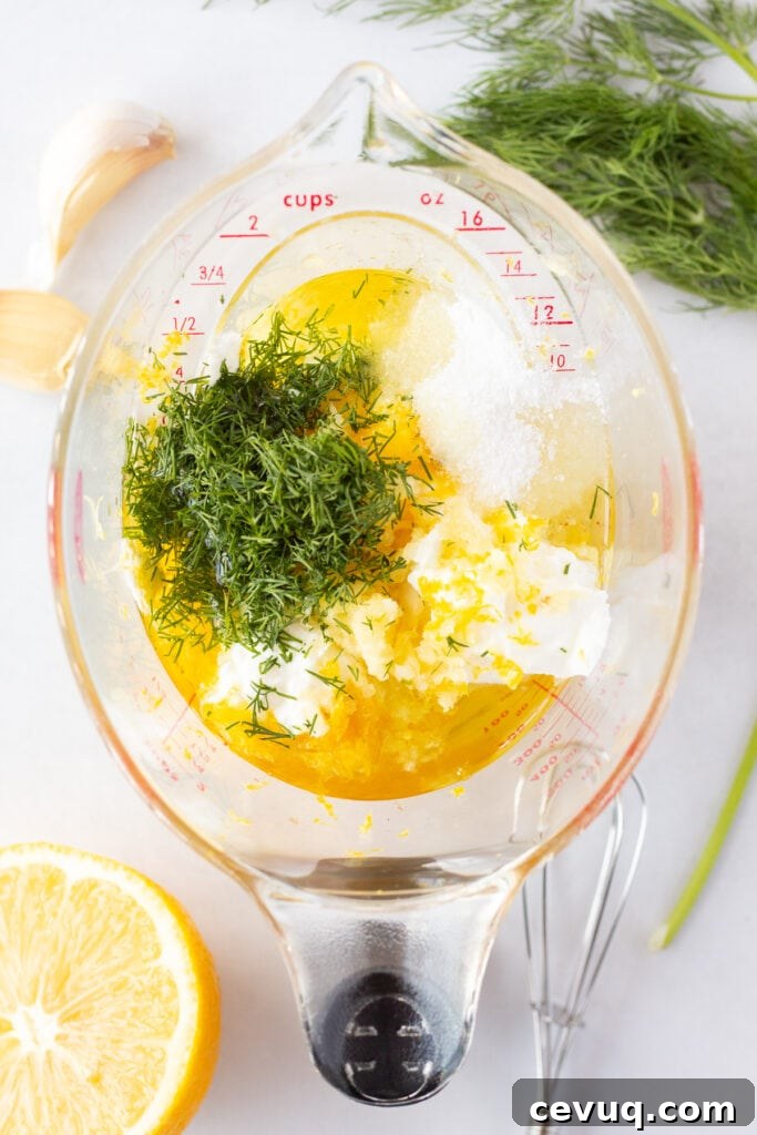 Ingredients for a Greek yogurt marinade, including fresh dill, garlic, lemon juice and zest, and kosher salt, in a measuring cup.