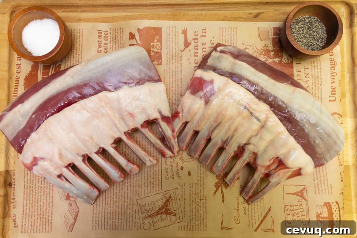 Two racks of lamb on wood cutting board with a small dish with salt and pepper.