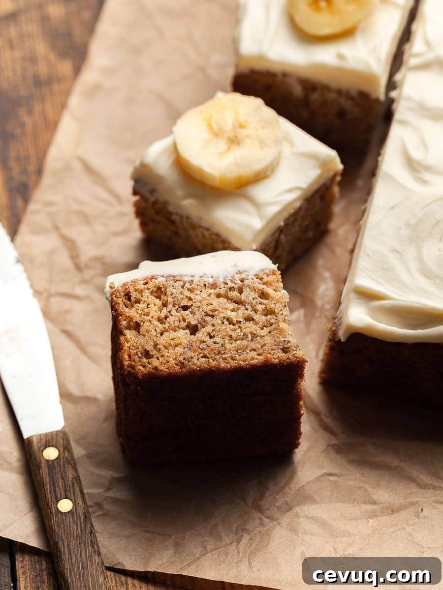 gluten free banana bars topped with cream cheese frosting and fresh bananas. on parchment paper with a small knife on the side