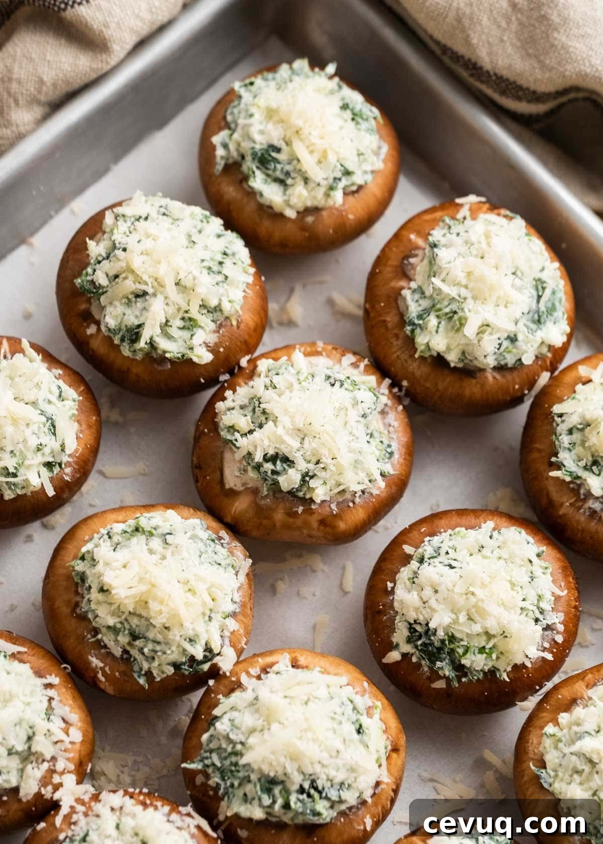 raw mushrooms stuffed with cheesy spinach mixture on a baking pan