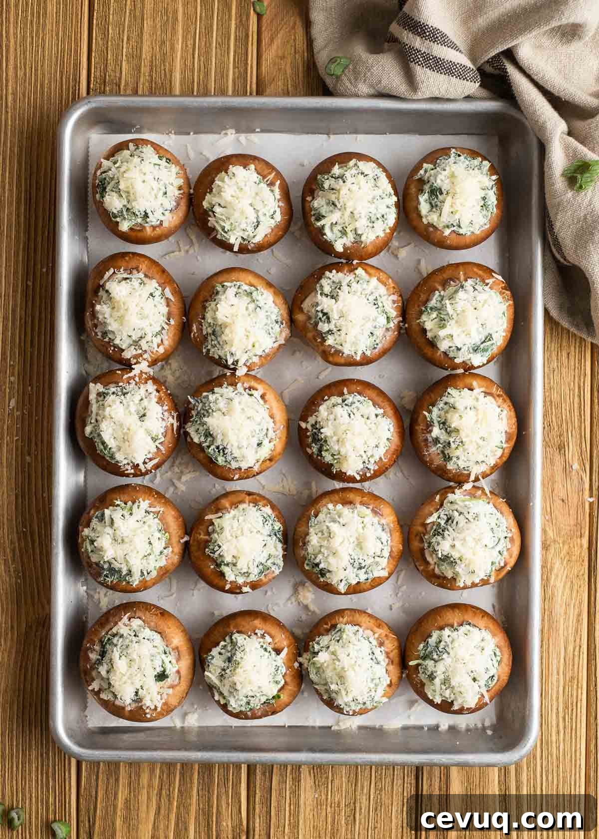 spinach stuffed mushrooms topped with parmesan cheese on a lined baking pan