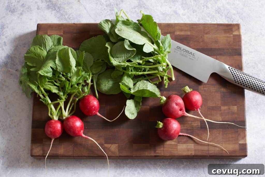 Radishes with greens and a chef's knife on a cutting board.