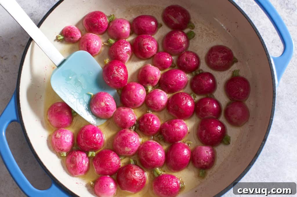 Cooked radish halves in an enamel pan with a spatula.