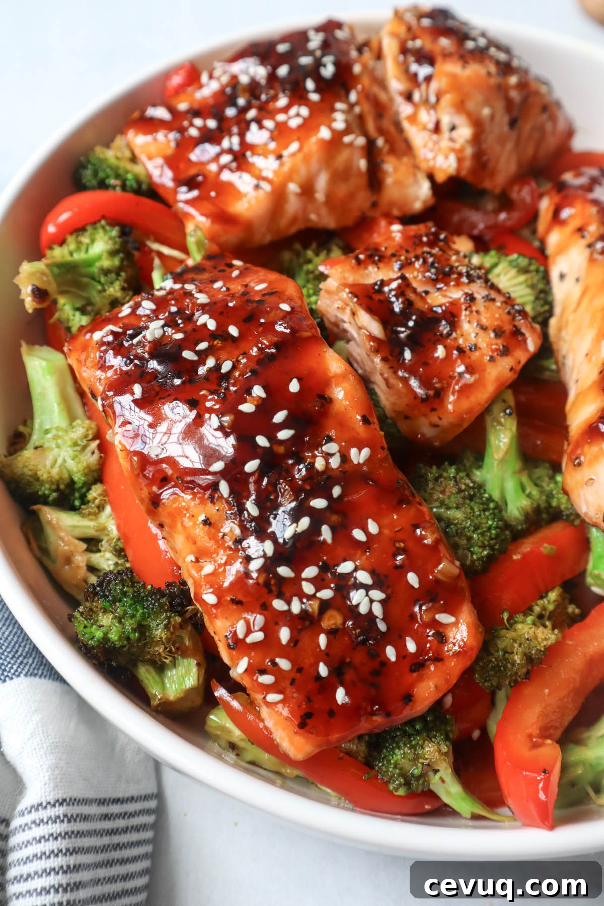 white bowl with red bell pepper, broccoli, cooked salmon topped with sauce and sesame seeds