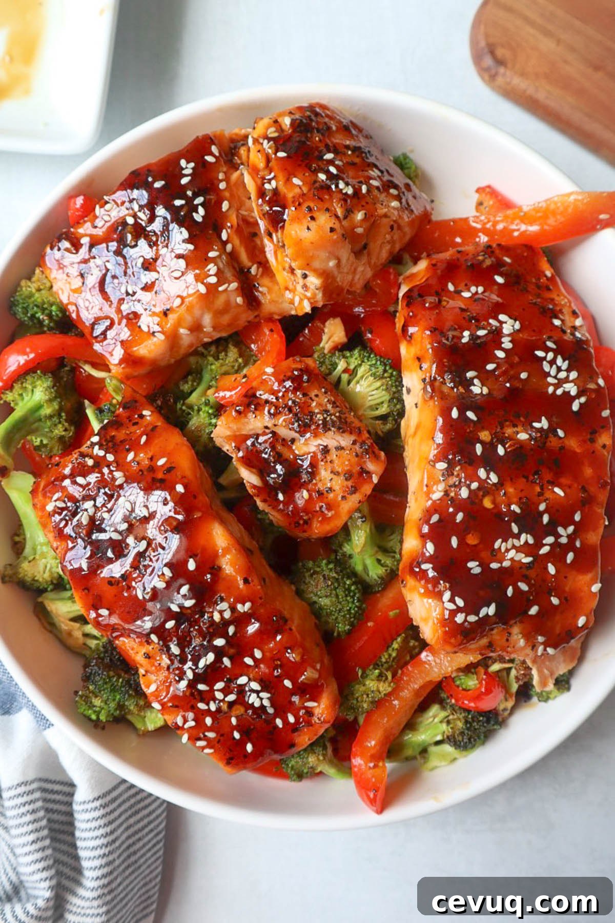 white bowl with red bell pepper, broccoli, cooked salmon topped with sauce and sesame seeds