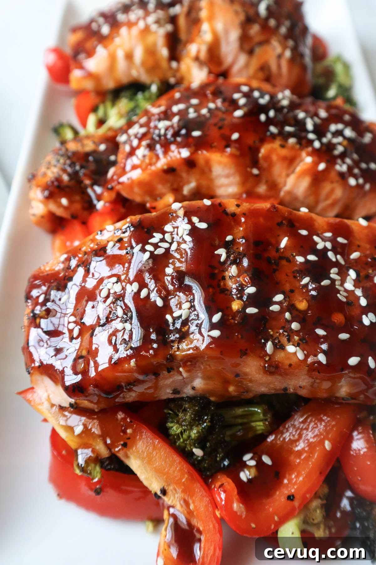 white plate with red bell pepper, broccoli, cooked salmon topped with sauce and sesame seeds