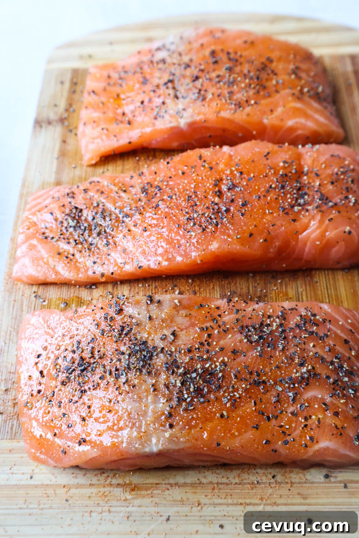 wooden cutting board with seasoned raw salmon filets