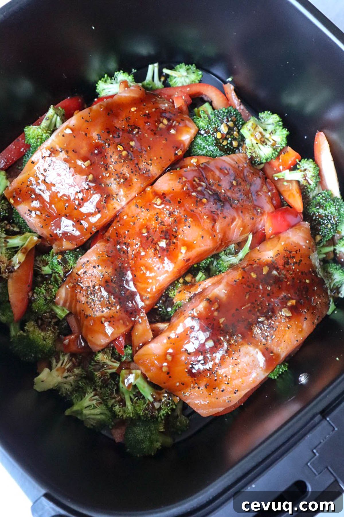 air fryer basket with red pepper, broccoli, and salmon filets topped with sauce