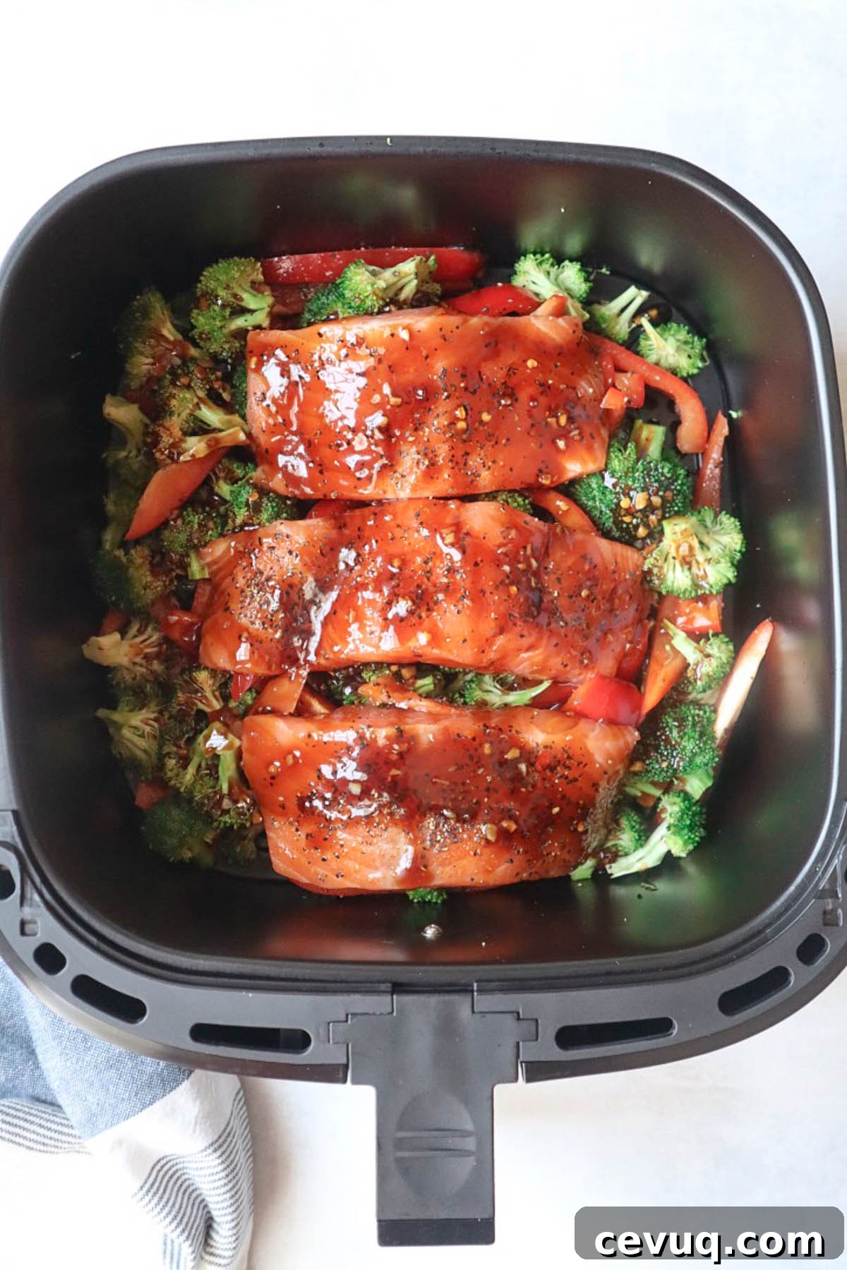 air fryer basket with vegetables and raw salmon with sauce poured over top