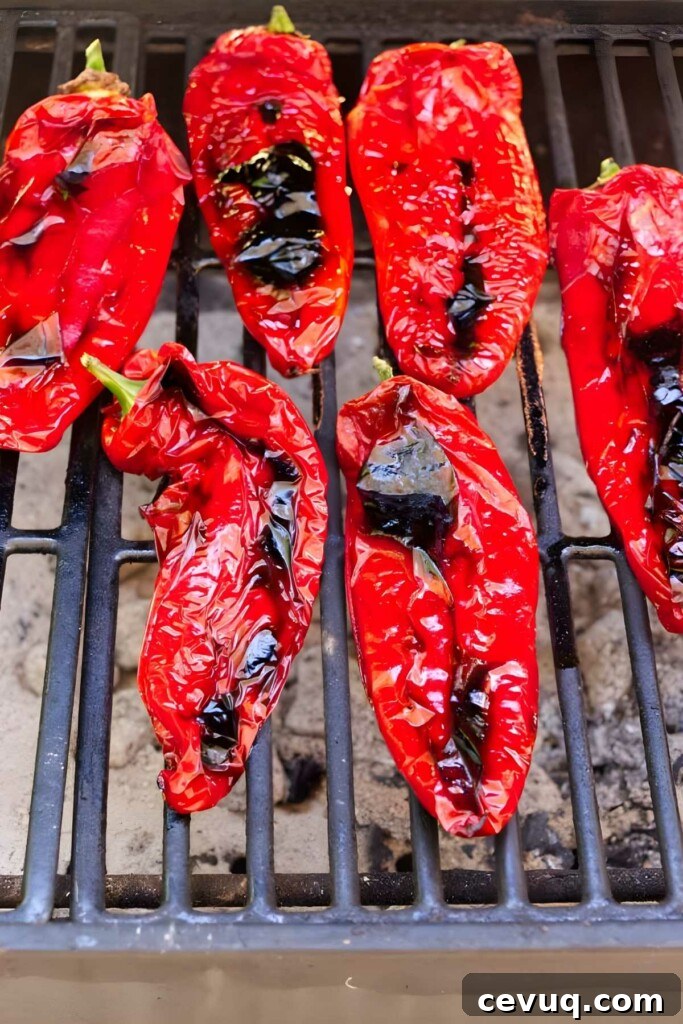 Several red peppers on a grill over coals.