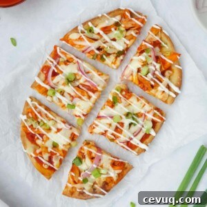 Whole buffalo chicken flatbread topped with green onions, red onions, and a drizzle of sour cream displayed on parchment paper on a white counter
