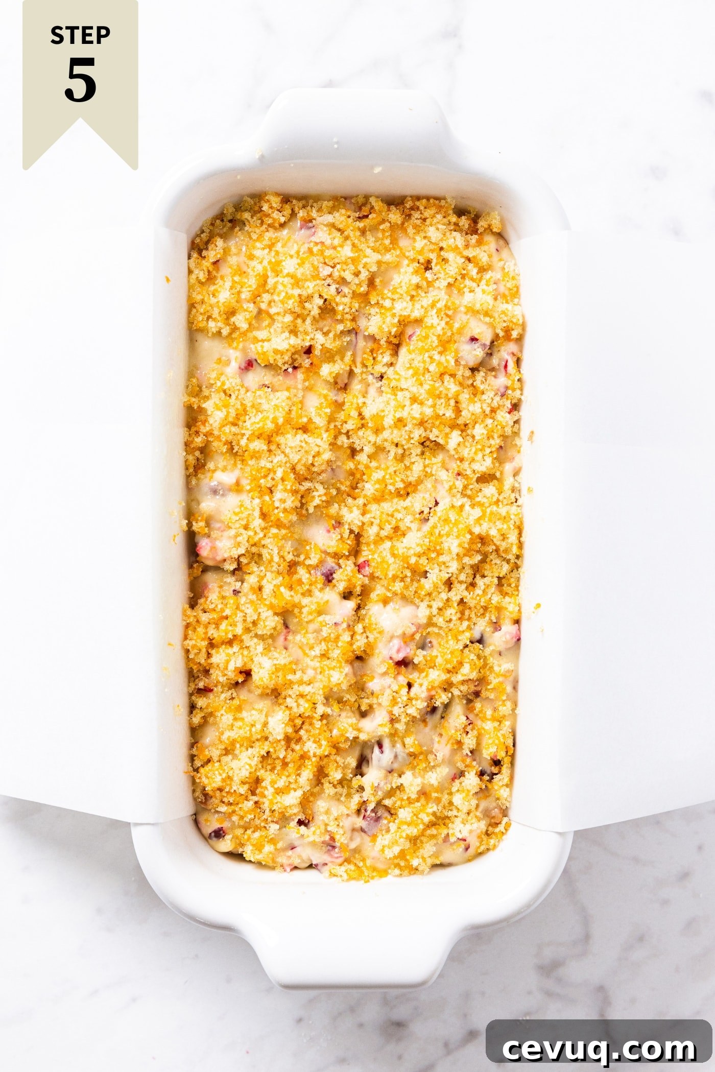 White rectangular loaf pan filled with unbaked cranberry orange bread batter sitting on marble surface.