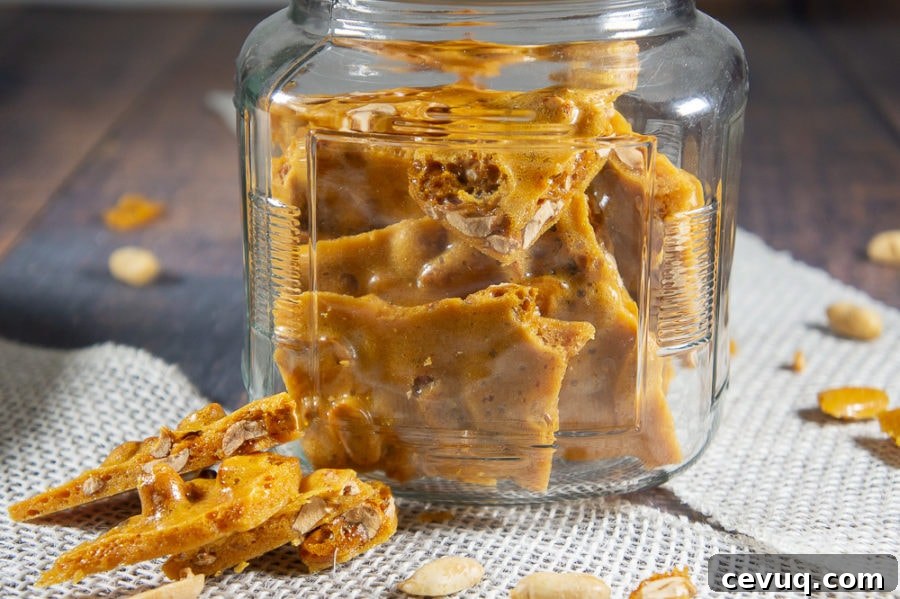 a jar of peanut brittle with a few pieces taken out on a wooden table.
