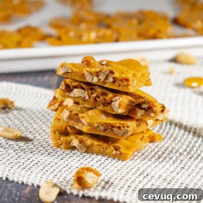 Four pieces of peanut brittle stacked on a burlap sheet on a wooden table with scattered peanuts and brittle around it