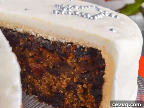 A dark fruit cake with a slice cut out and a layer of marzipan and royal frosting