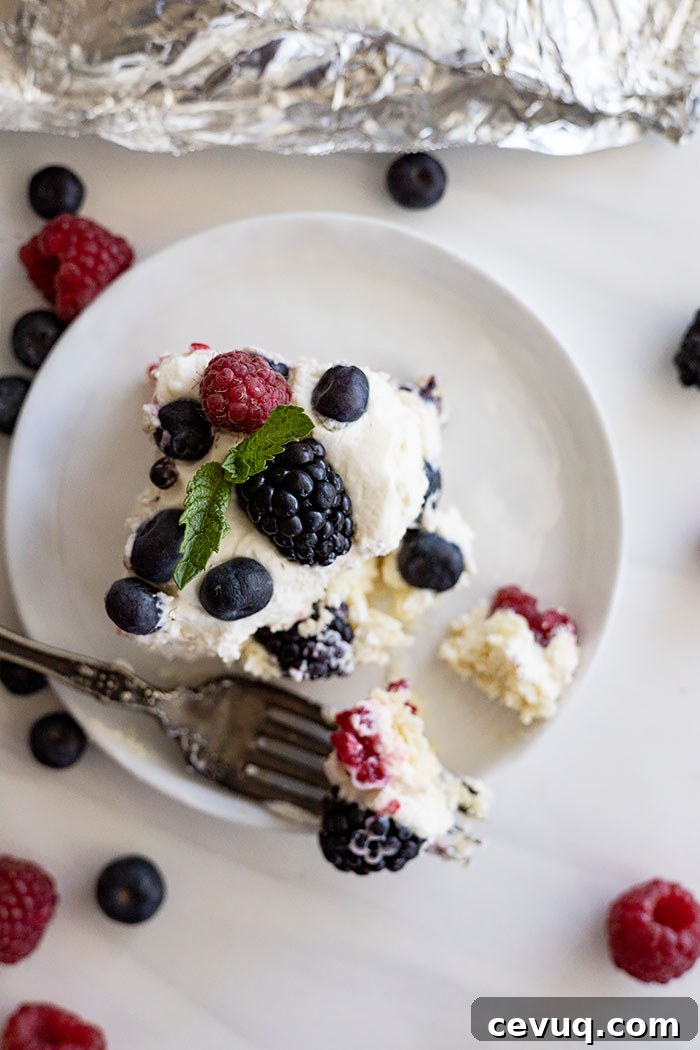 No Bake Berry Icebox Cake with Fresh Berries 6 Overhead view of a piece of cake on a white plate with berries scattered around.