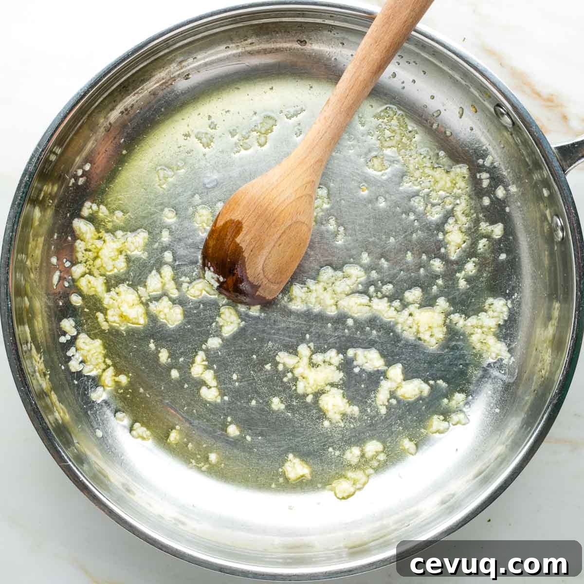 Vegan White Bean Puttanesca Pasta 5 Crushed garlic in olive oil, pushed around by a wooden spoon in a skillet.