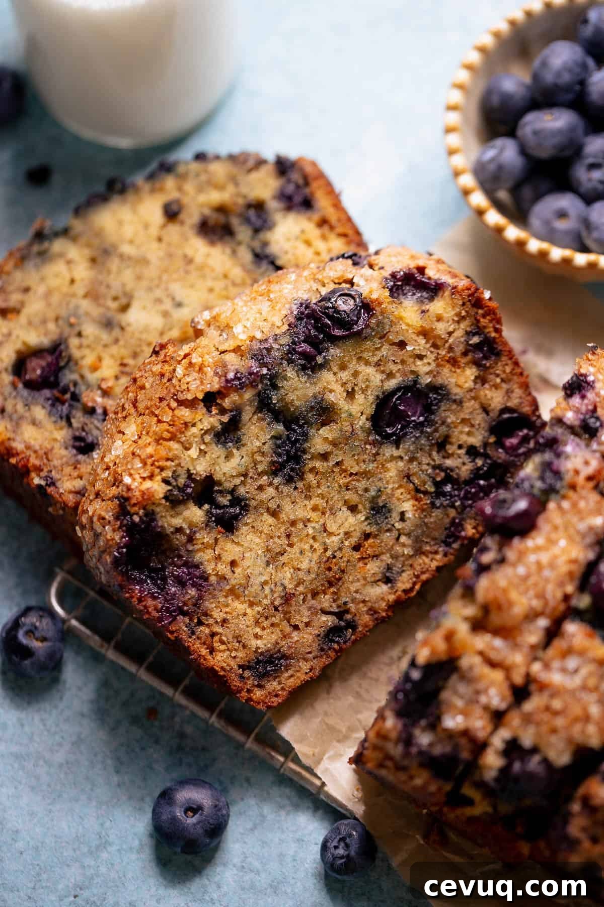 Sliced blueberry banana bread served with a glass of milk and fresh blueberries.