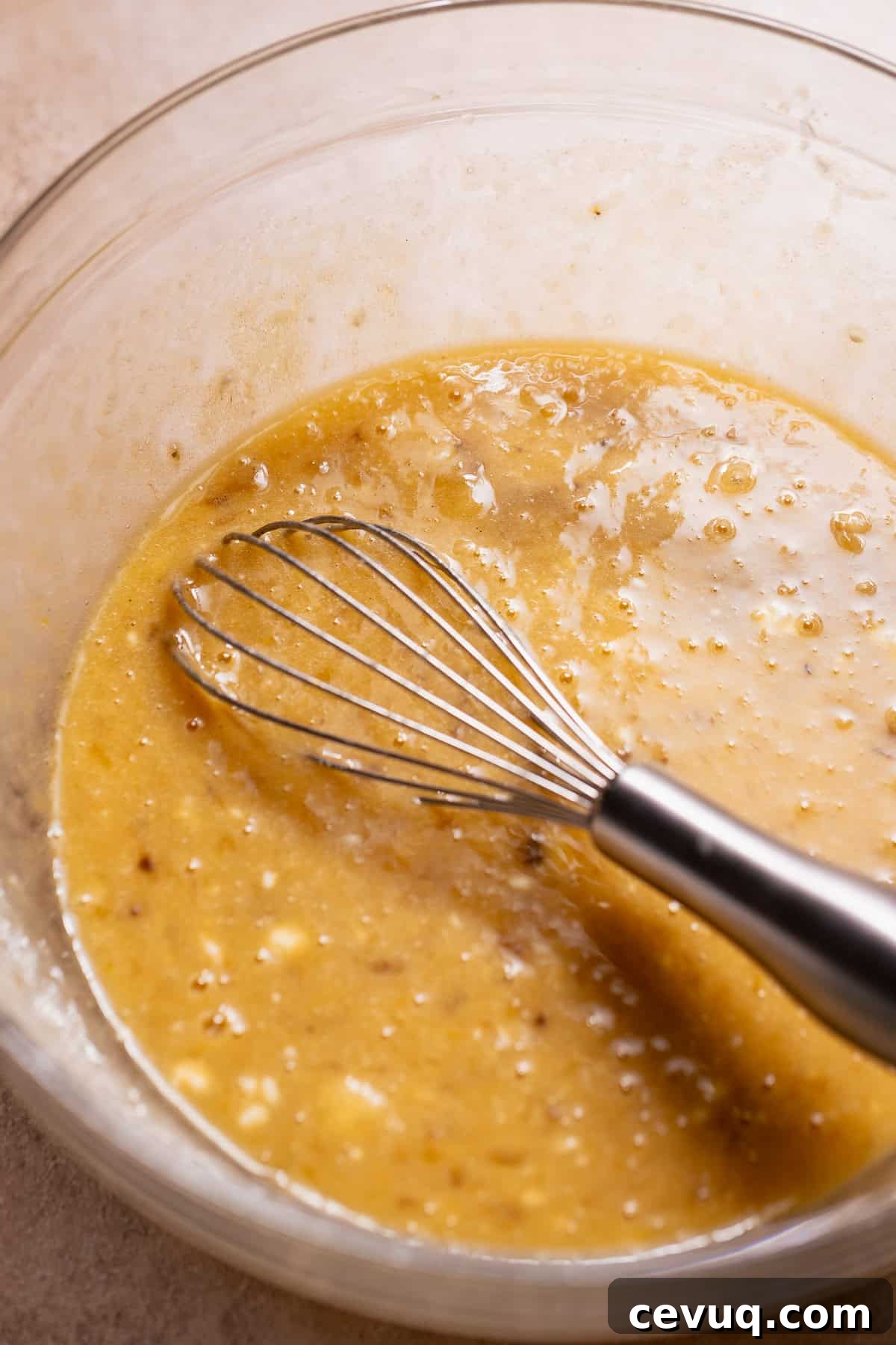 Whisking mashed bananas with wet ingredients for blueberry banana bread batter.