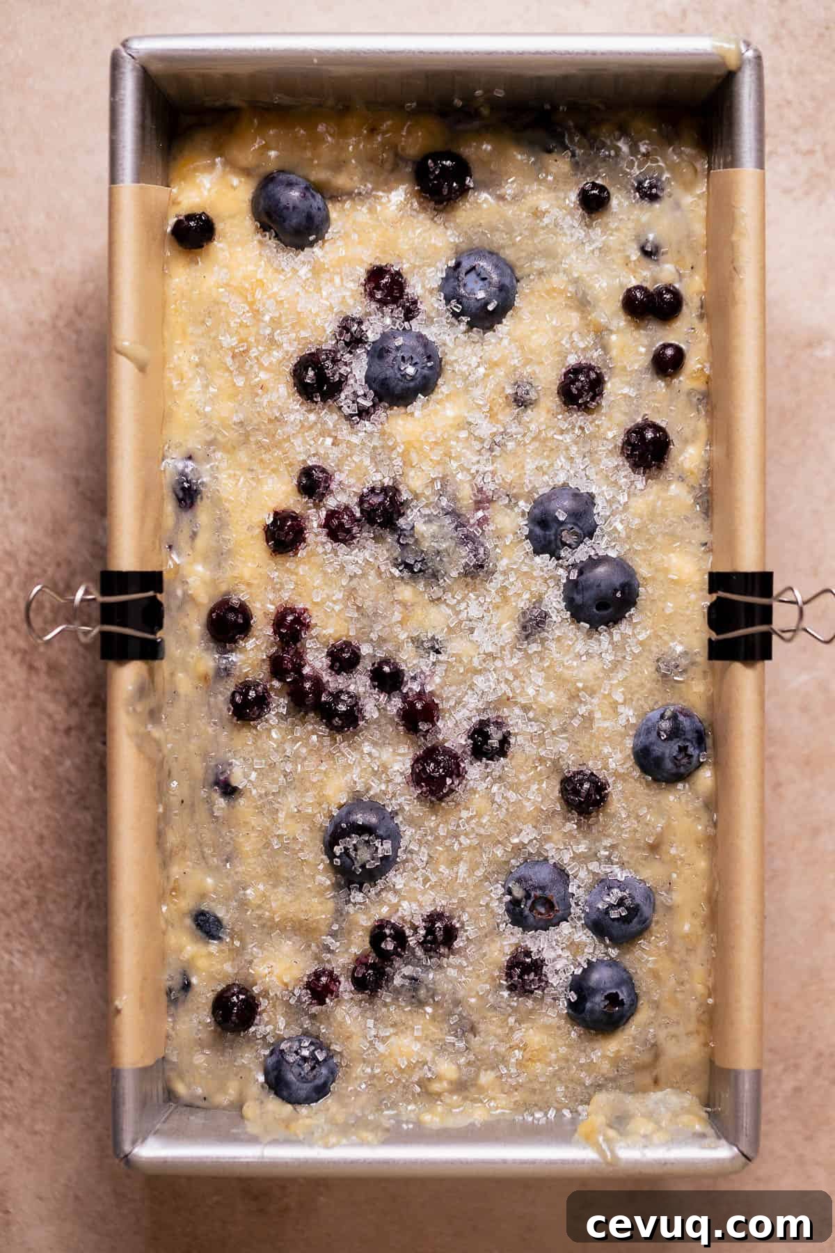 Unbaked blueberry banana bread batter in a lined loaf pan topped with sugar and berries.