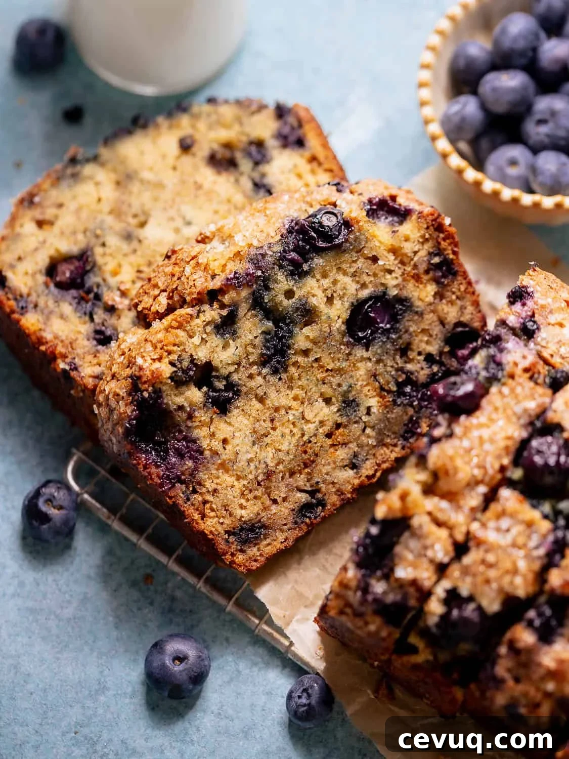 Slices of blueberry banana bread on parchment paper with fresh blueberries nearby.