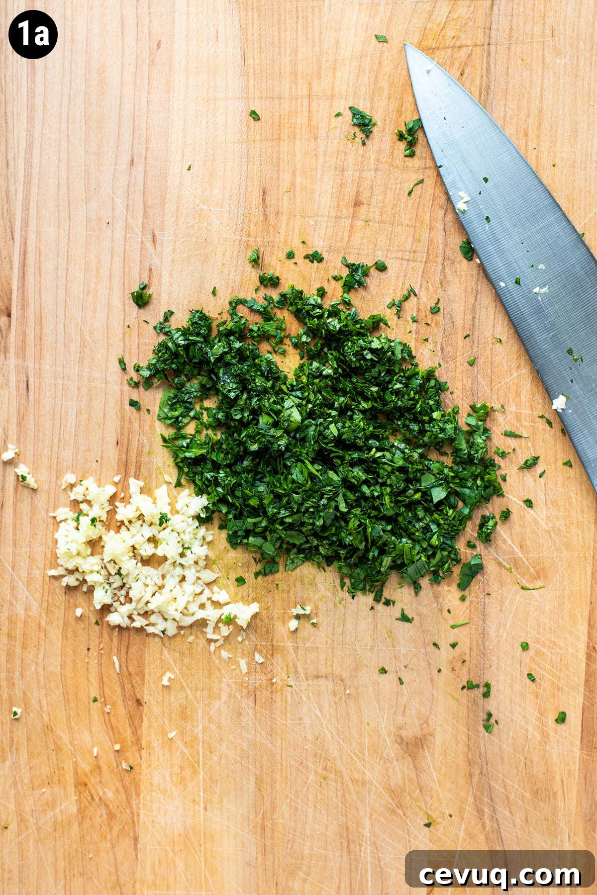 Minced garlic, parsley, and cilantro on a wooden cutting board.