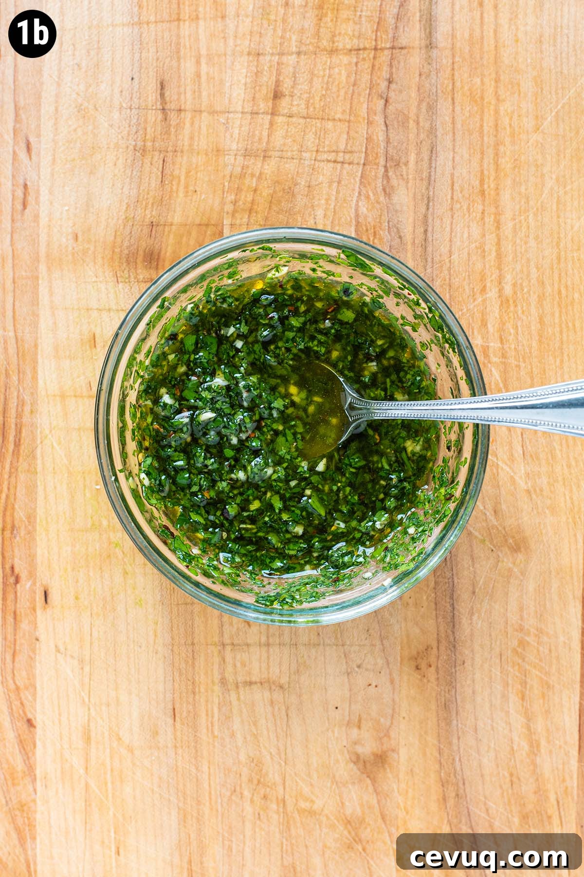 Chimichurri sauce in a small glass bowl on a wooden cutting board.