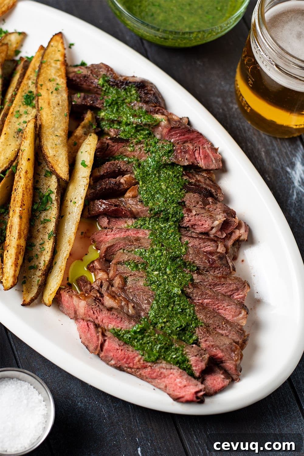 Perfect medium rare ribeye steak sliced into thin strips on a plate and topped with a generous serving of chimichurri sauce.