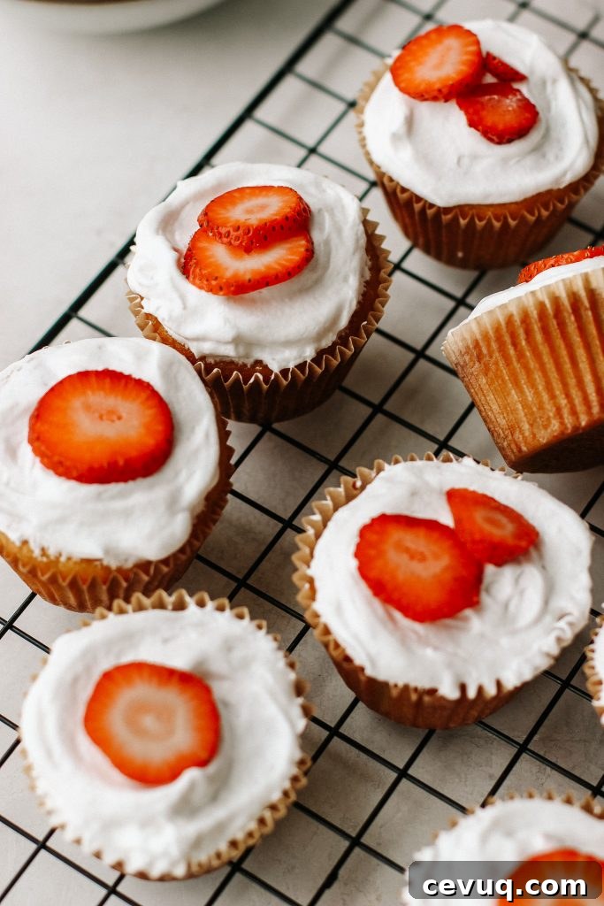 Paleo Strawberry Shortcake Cupcakes Recipe 4 strawberry shortcake cupcakes on a cooling rack with a bowl of strawberries and bowl of cool whip