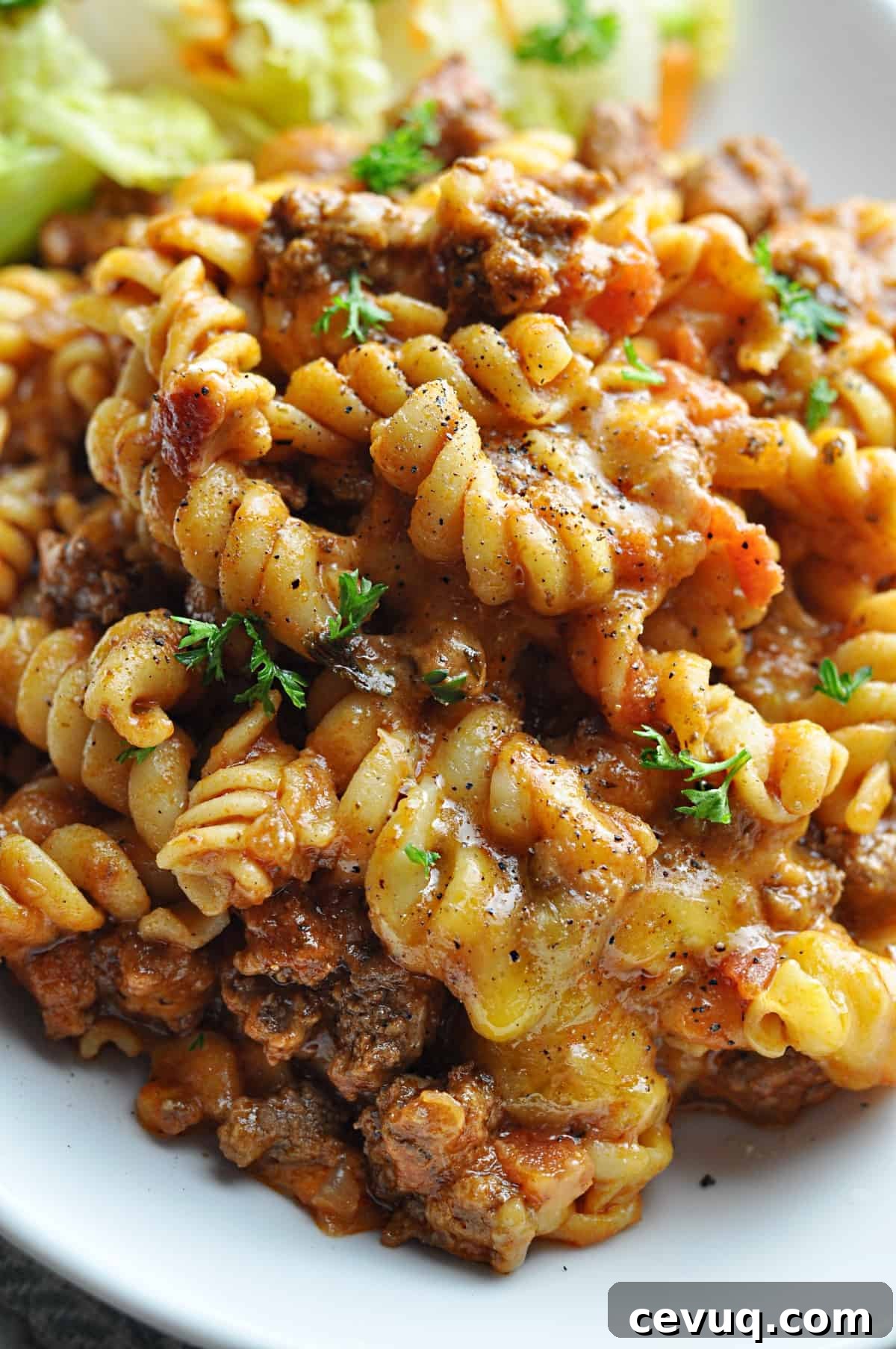 Rotini pasta with ground beef, tomato sauce, and melted cheese served on plate.