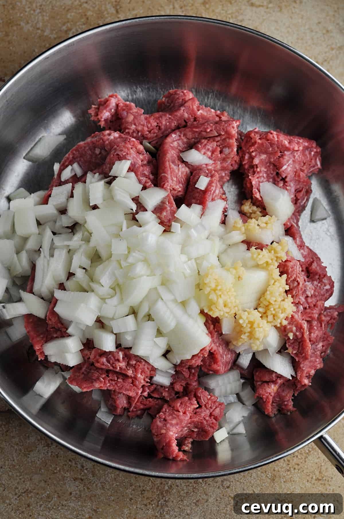 Uncooked ground beef, chopped onion, and minced garlic in skillet ready to cook.