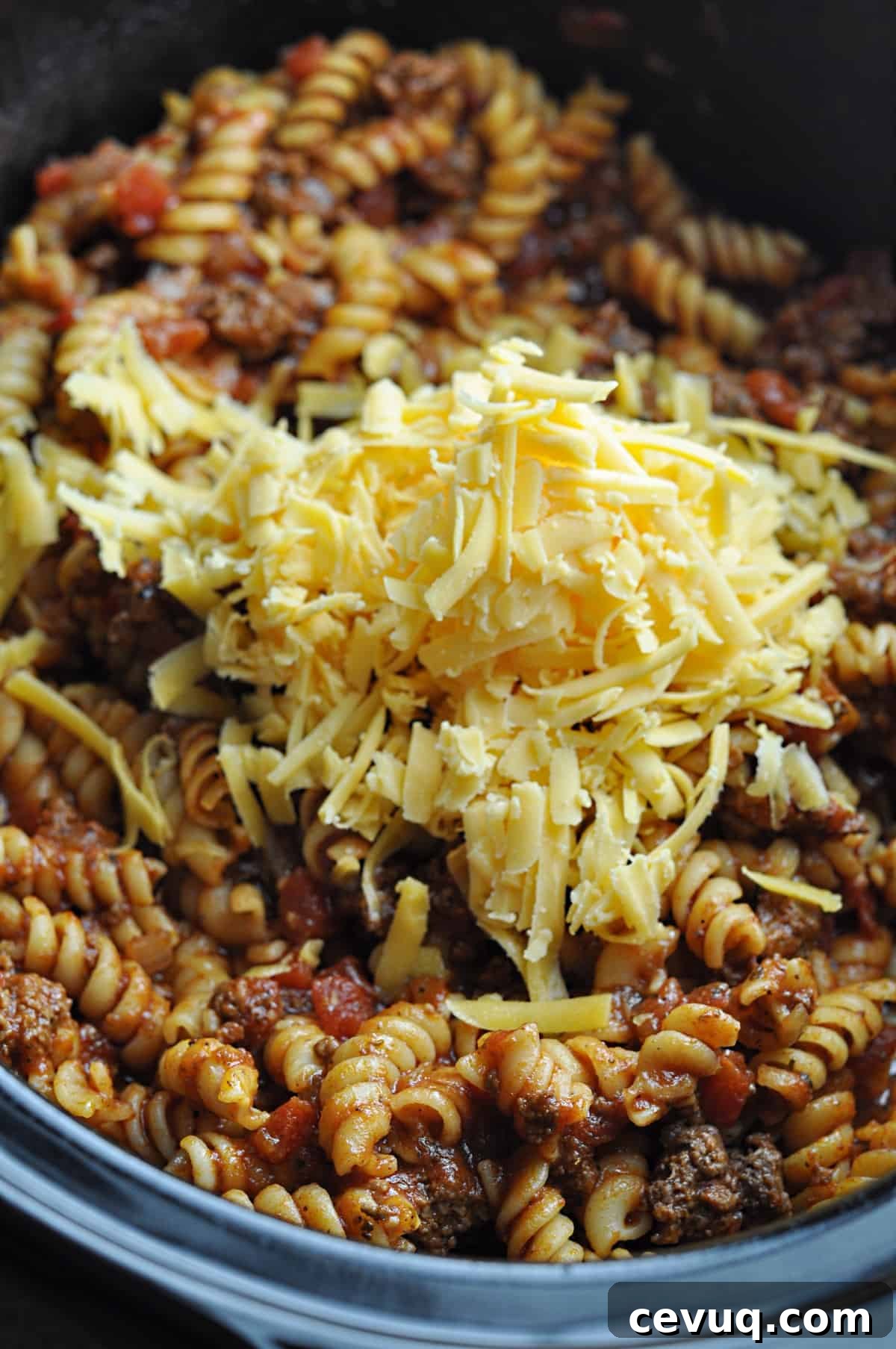 Cooked goulash with ground beef with unmelted cheese on top in slow cooker.