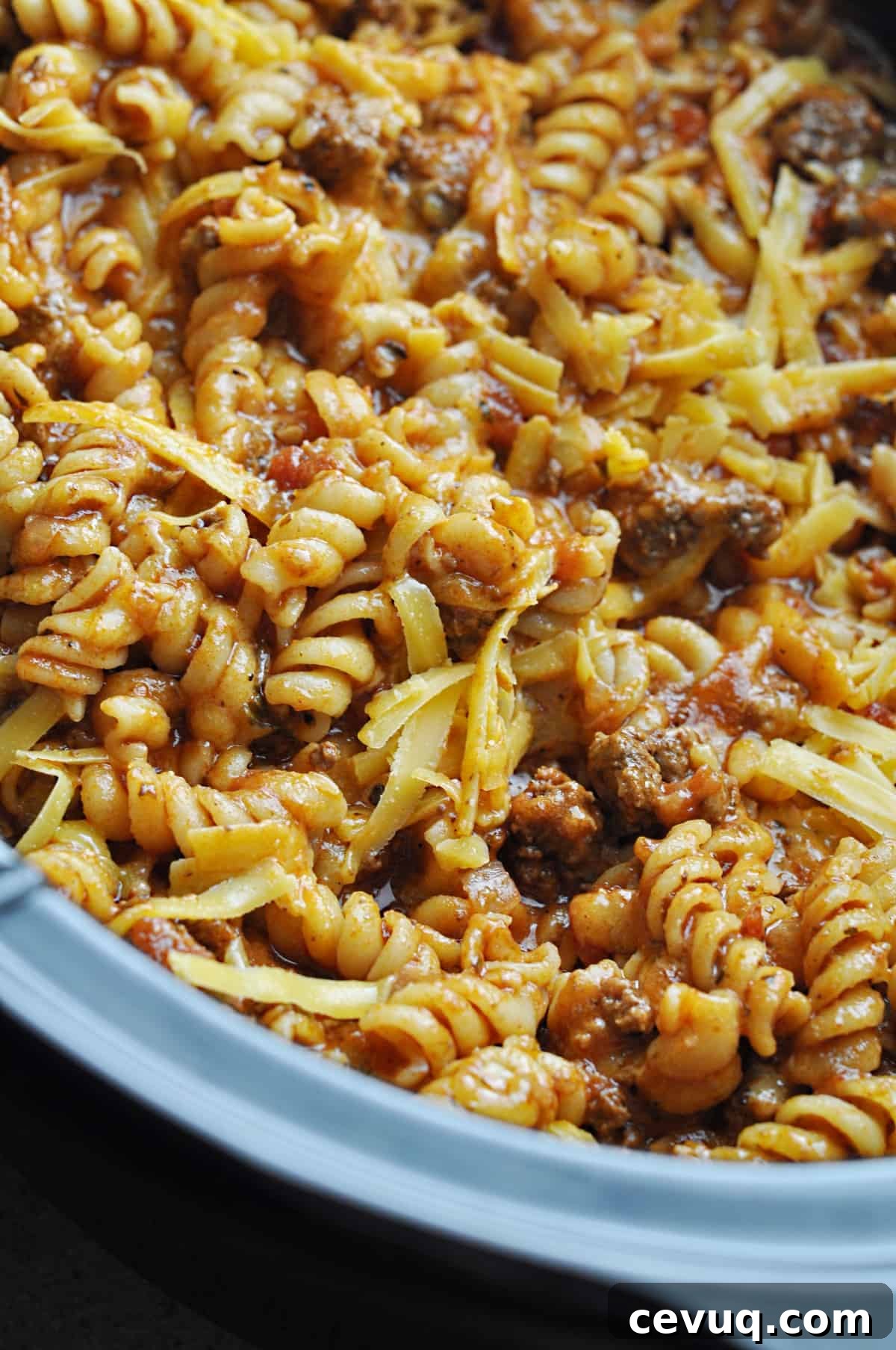 Rotini pasta with ground beef and cheese and spices cooking in slow cooker.