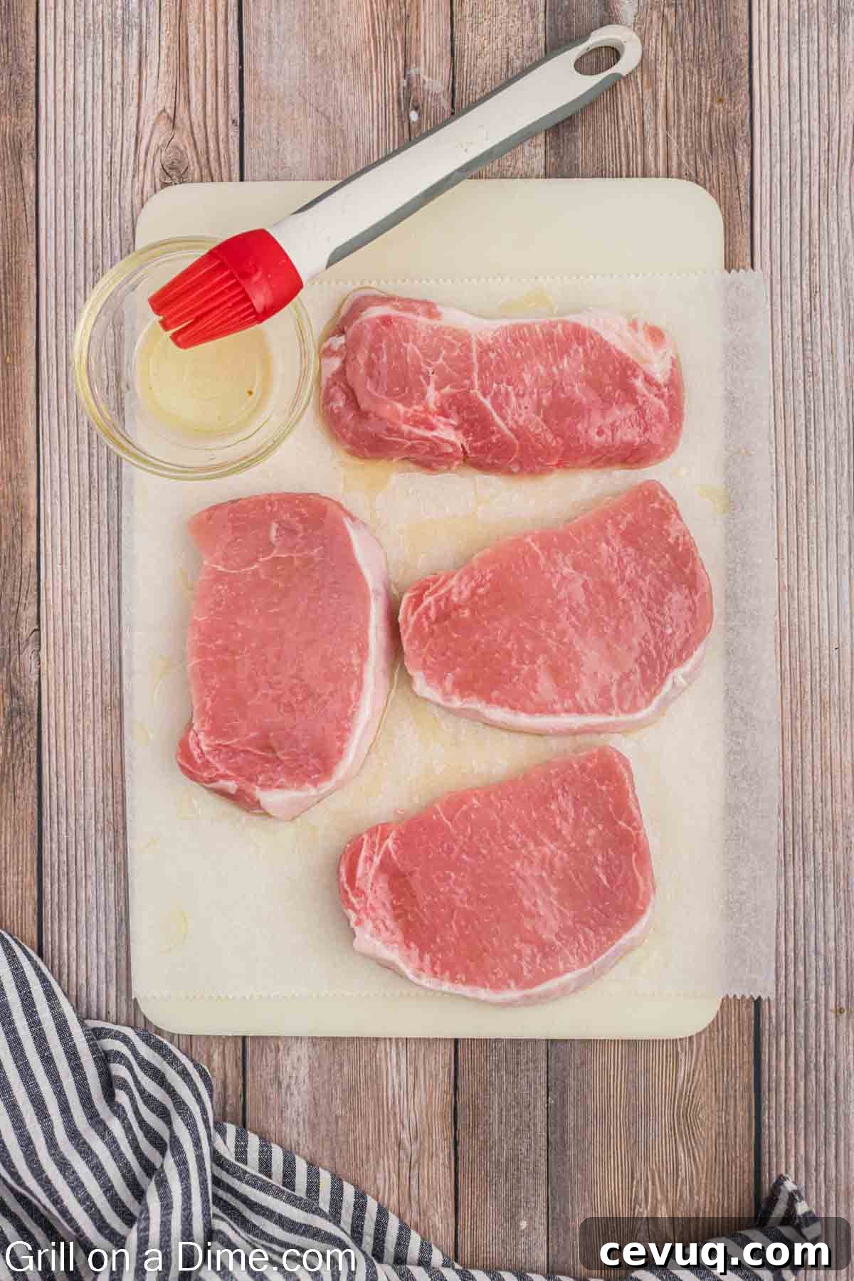 Uncooked pork chops on a cutting board being basted with oil