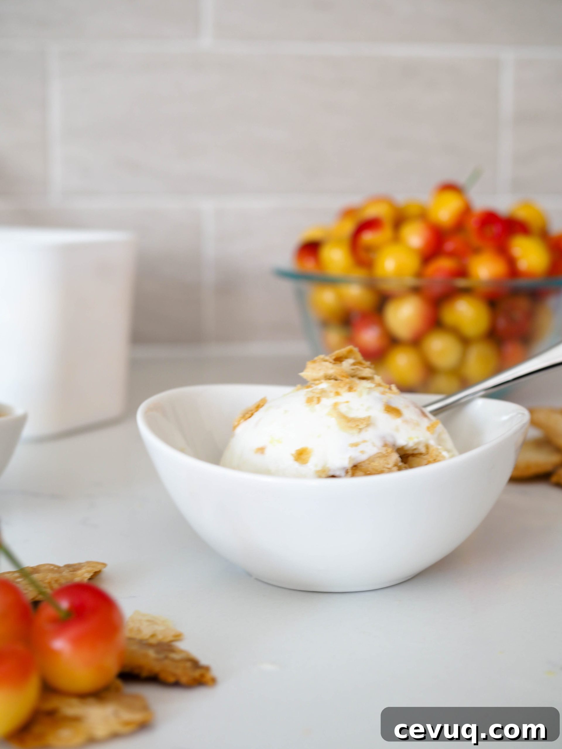 Closeup of a bowl of cherry pie ice cream with Rainier cherries in the background.