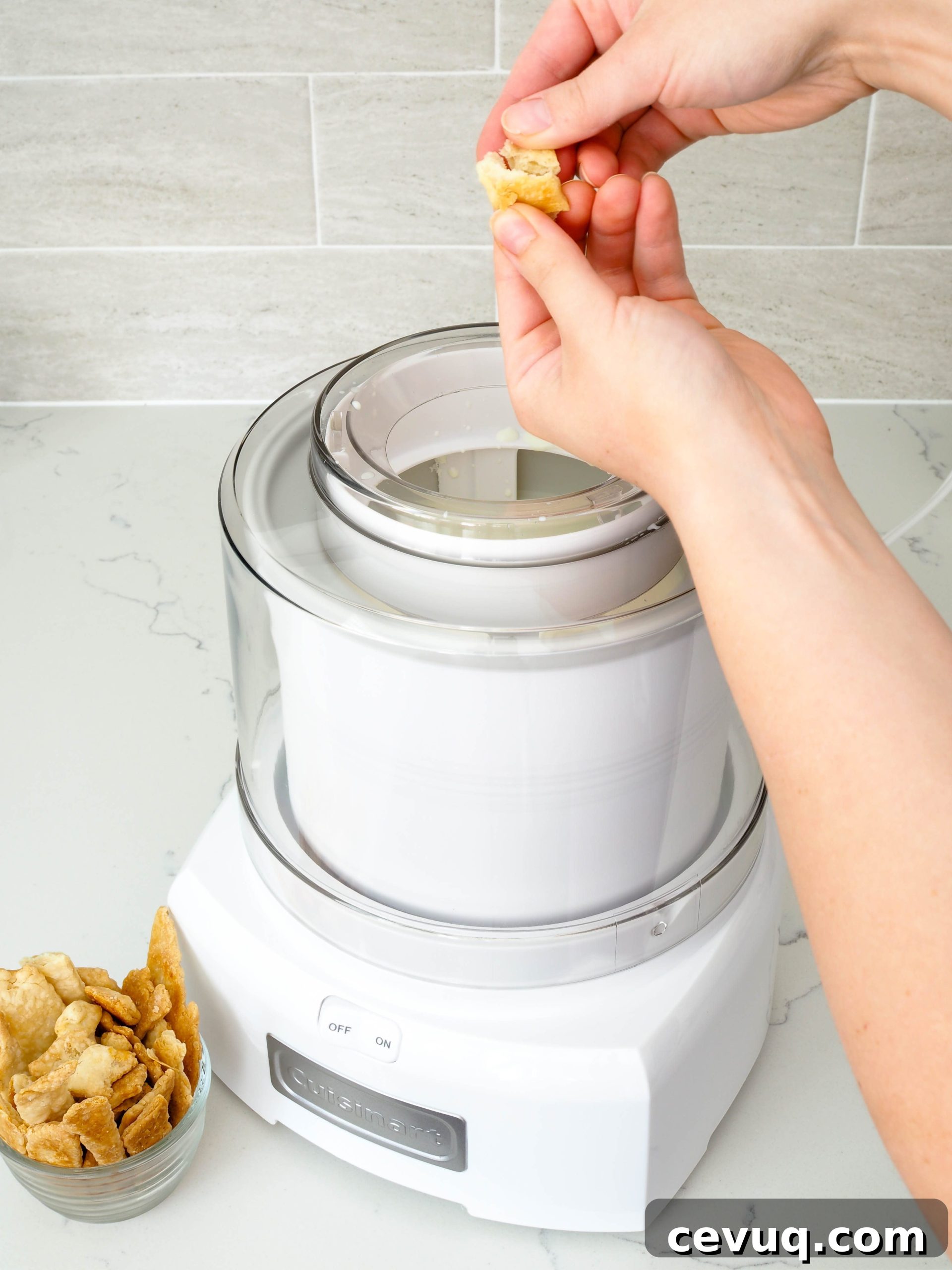 Two white hands break up a piece of baked pie crust above an ice cream canister.