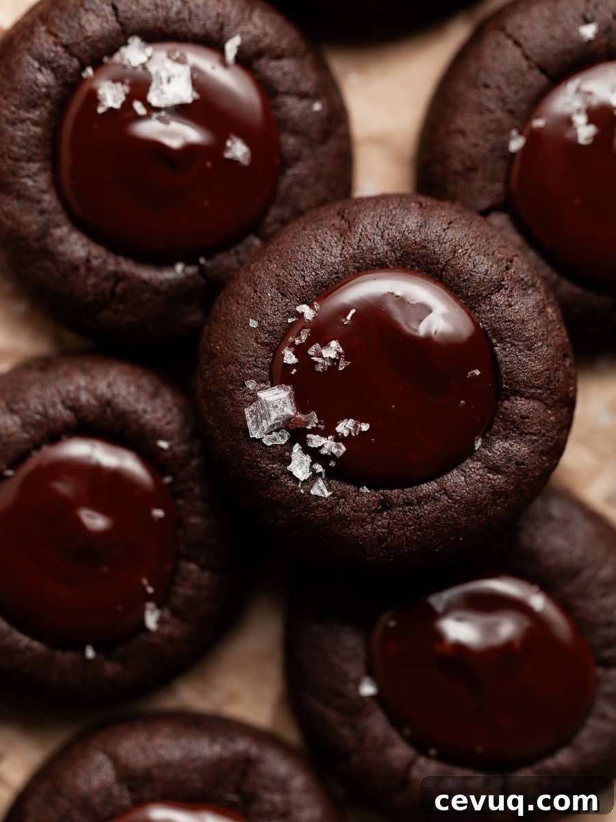 chocolate thumbprint cookies with dark chocolate ganache filling and a sprinkle of sea salt on brown parchment paper
