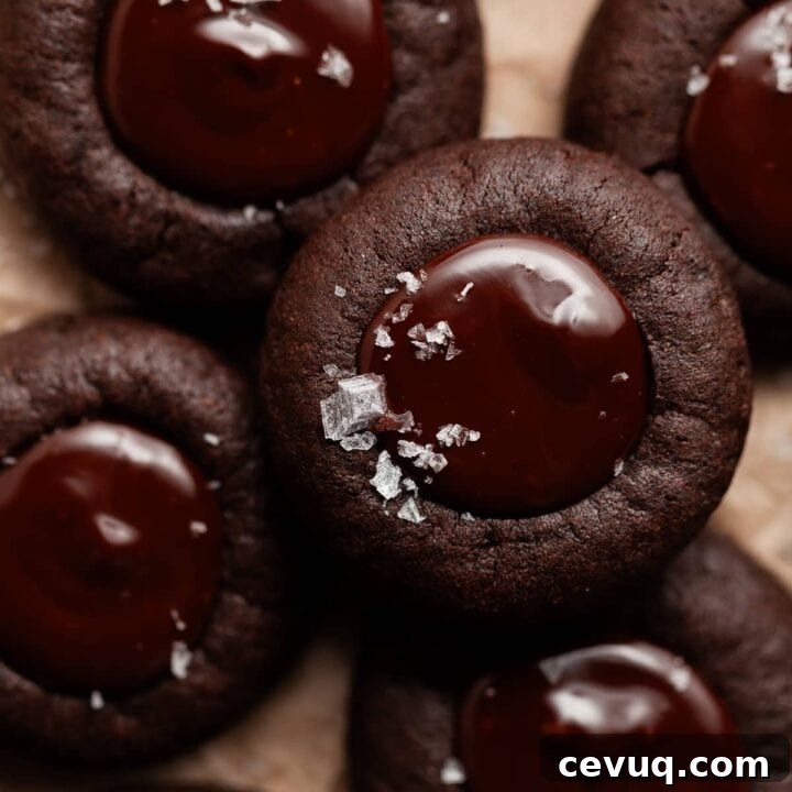 gluten free chocolate thumbprint cookies with dark chocolate ganache filling and a sprinkle of sea salt on brown parchment paper