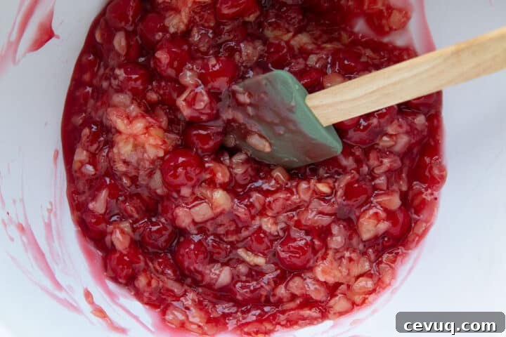 cherry pie filling and crushed pineapple mixed in a white bowl with a spatula.