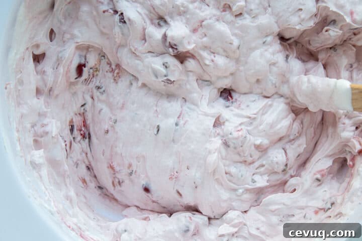 fluffy pink whipped topping mixture with flecks of cherries in a white bowl.